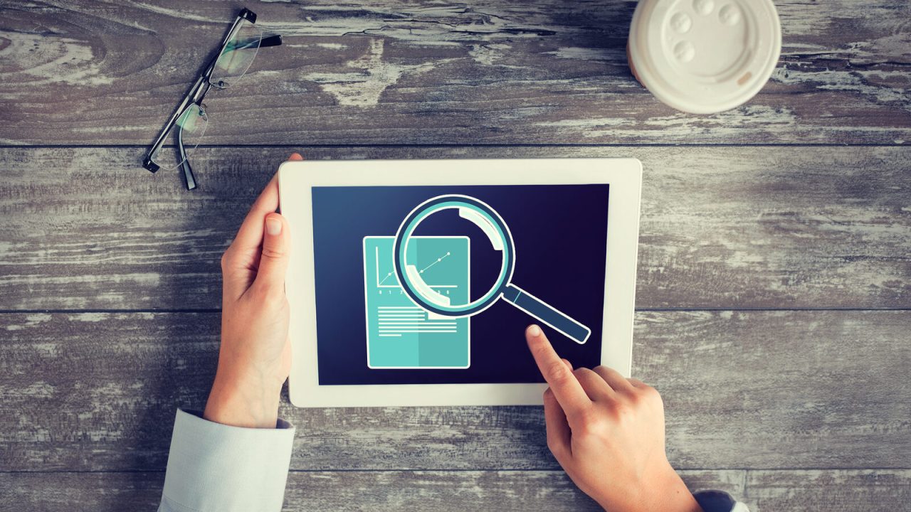 Hands reviewing a tablet dashboard with a magnifier and graph