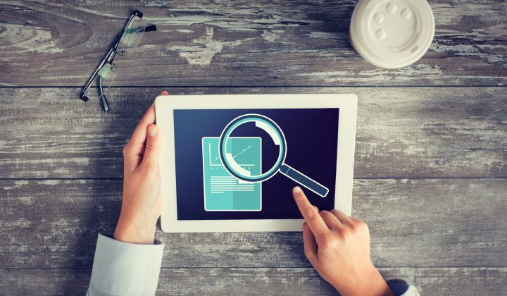 Hands reviewing a tablet dashboard with a magnifier and graph